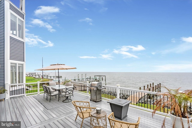 wooden terrace featuring outdoor dining space, a grill, and a water view