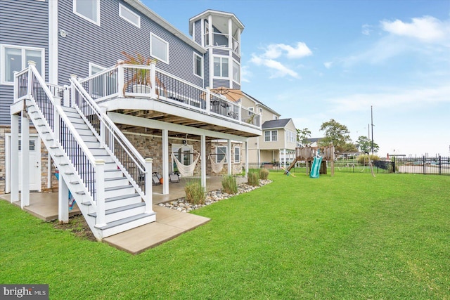 back of property with a playground, a wooden deck, a lawn, and a patio area