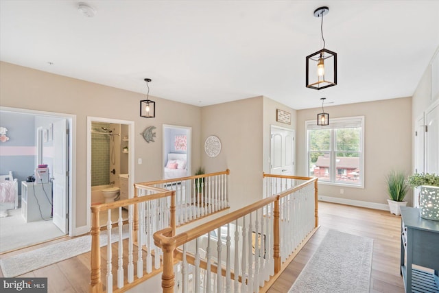 hallway with baseboards, an upstairs landing, and light wood-style flooring