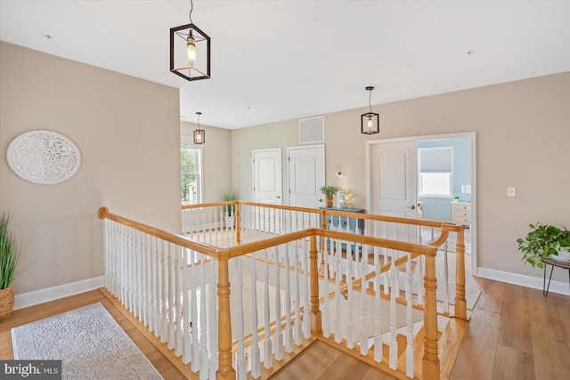 hall featuring baseboards, an upstairs landing, visible vents, and wood finished floors