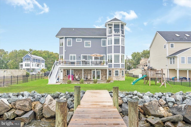 back of property with a lawn, stone siding, a fenced backyard, a playground, and stairway