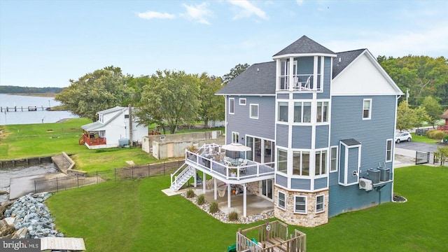 back of house featuring fence, a deck with water view, a yard, a shingled roof, and stone siding