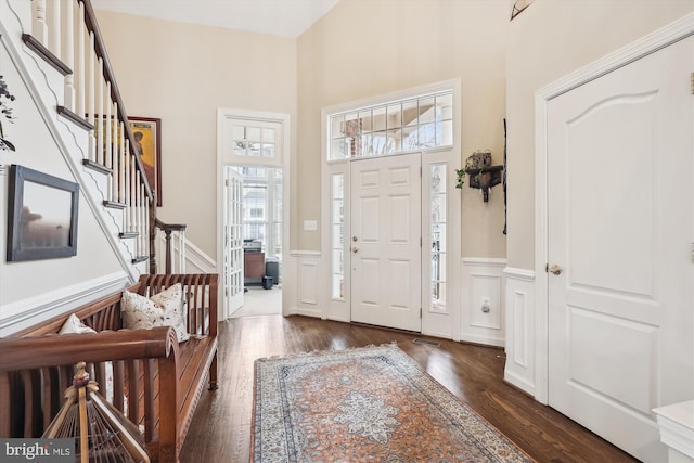 entryway featuring wood finished floors, stairway, wainscoting, a decorative wall, and a towering ceiling