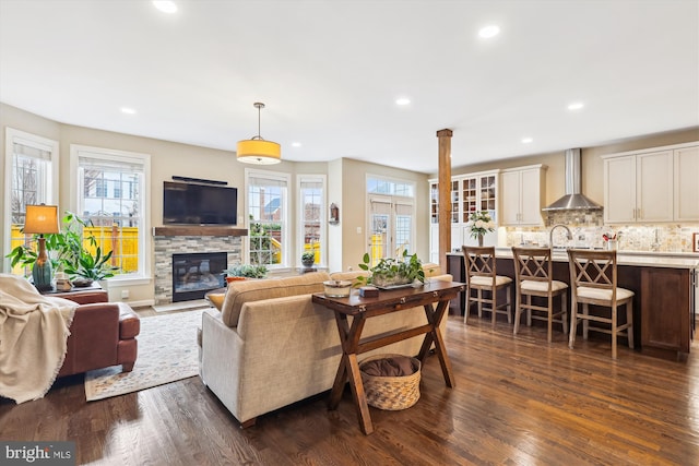 living room with a stone fireplace, recessed lighting, and dark wood-style floors