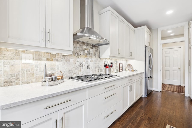 kitchen with decorative backsplash, white cabinetry, stainless steel appliances, and wall chimney exhaust hood