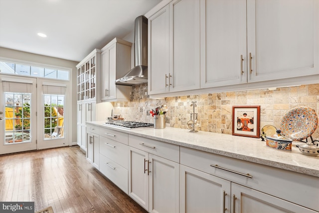 kitchen featuring hardwood / wood-style floors, light stone countertops, stainless steel gas stovetop, wall chimney exhaust hood, and backsplash