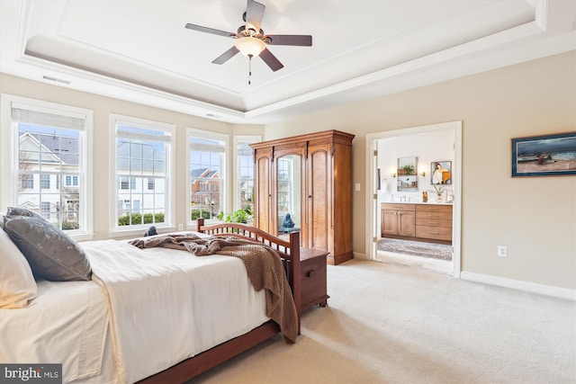 bedroom featuring a raised ceiling, connected bathroom, baseboards, and light carpet