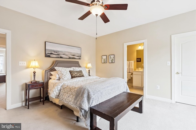 bedroom with ceiling fan, baseboards, light colored carpet, and ensuite bath