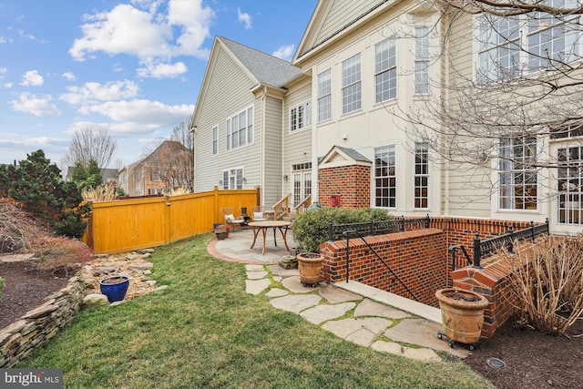 rear view of house featuring brick siding, a patio area, a yard, and fence