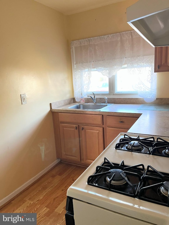 kitchen with white range with gas stovetop, light hardwood / wood-style floors, extractor fan, and sink