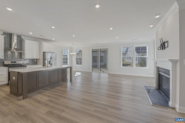 kitchen featuring wall chimney exhaust hood, sink, stainless steel appliances, a kitchen island with sink, and white cabinets