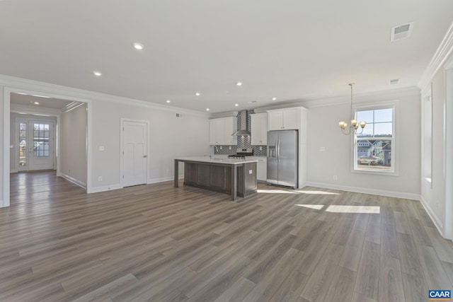 kitchen featuring white cabinetry, hanging light fixtures, a center island, stainless steel appliances, and wall chimney range hood