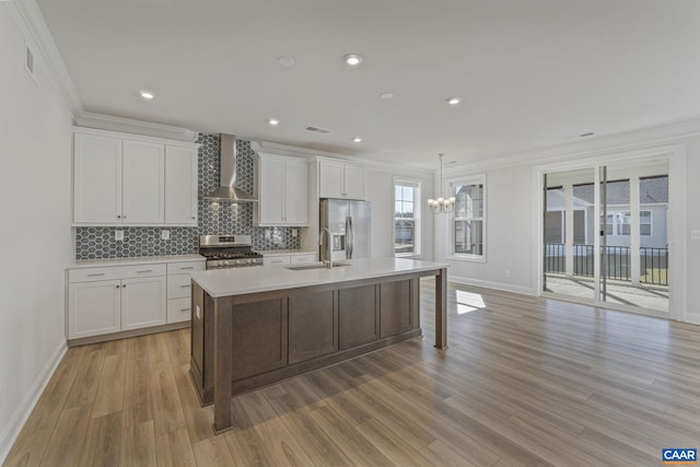 kitchen with appliances with stainless steel finishes, an island with sink, sink, white cabinets, and wall chimney exhaust hood