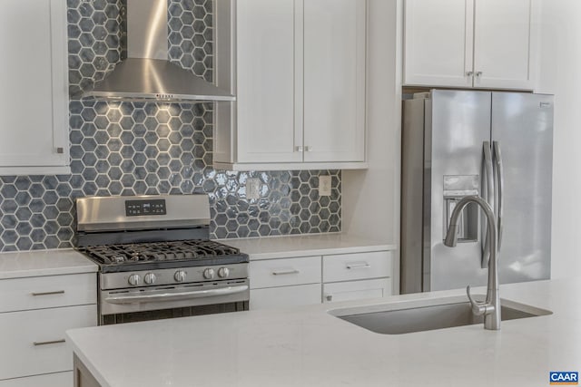 kitchen featuring sink, appliances with stainless steel finishes, wall chimney range hood, decorative backsplash, and white cabinets