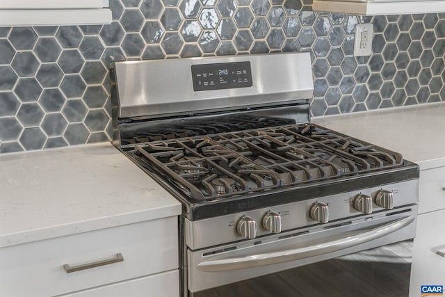 interior details with white cabinetry, gas range, and decorative backsplash