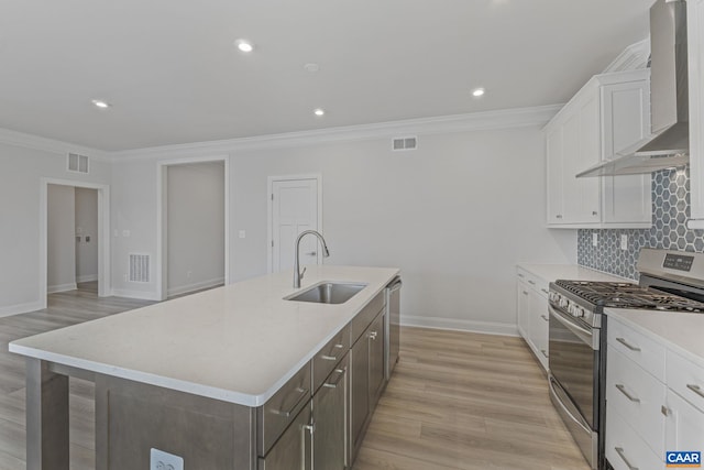 kitchen with appliances with stainless steel finishes, sink, white cabinets, a large island with sink, and wall chimney range hood