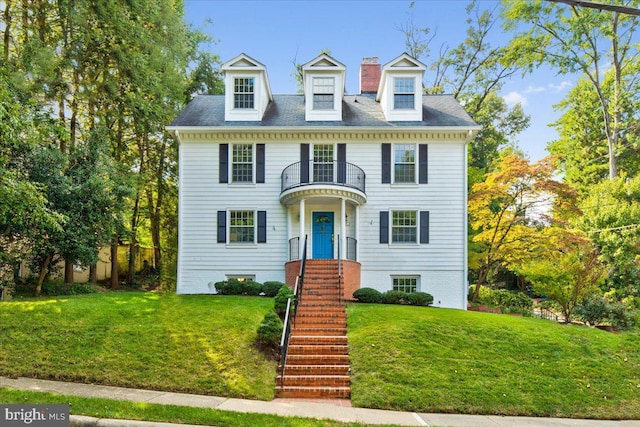 view of front facade featuring stairs, a front lawn, a chimney, and a balcony