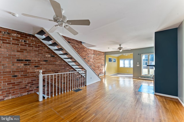 interior space with a baseboard heating unit, light hardwood / wood-style flooring, ceiling fan, and brick wall