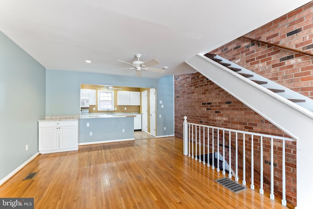 kitchen featuring brick wall, white cabinetry, sink, ceiling fan, and light hardwood / wood-style floors