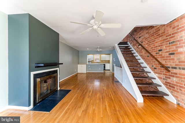 unfurnished living room featuring brick wall, ceiling fan, and light hardwood / wood-style floors