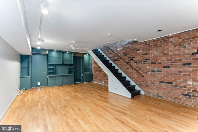 unfurnished living room featuring wood-type flooring, brick wall, and ceiling fan