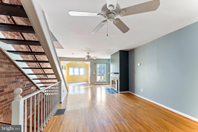 unfurnished living room featuring ceiling fan, brick wall, and light wood-type flooring