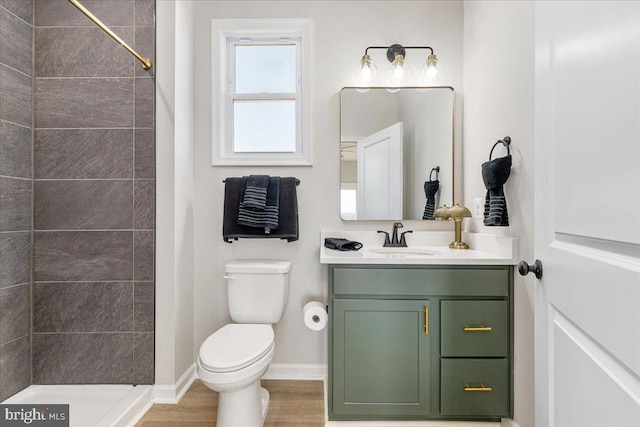 bathroom with tiled shower, vanity, toilet, and wood-type flooring