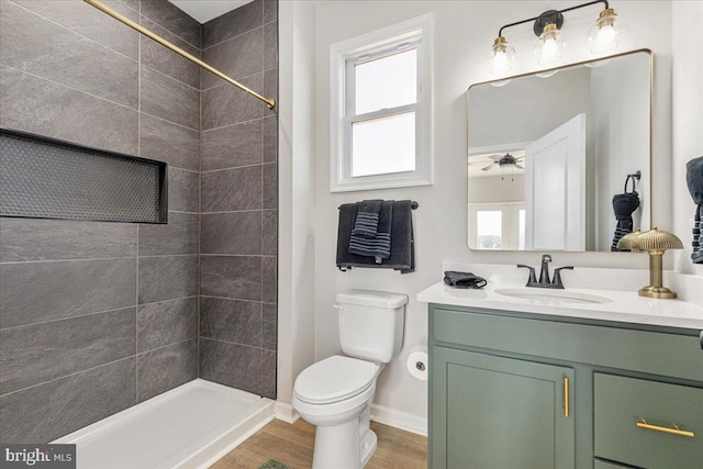 bathroom with ceiling fan, a tile shower, vanity, wood-type flooring, and toilet