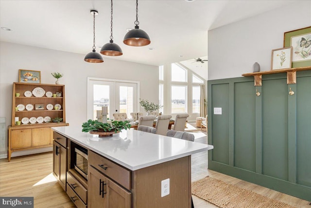 kitchen featuring hanging light fixtures, a kitchen island, stainless steel microwave, and light hardwood / wood-style flooring