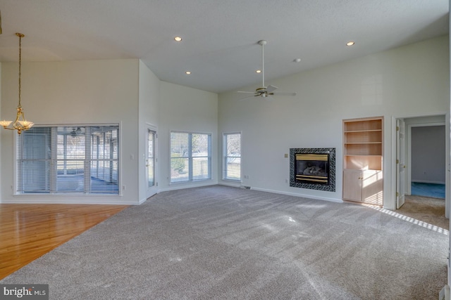 unfurnished living room featuring a premium fireplace, carpet floors, ceiling fan with notable chandelier, and high vaulted ceiling