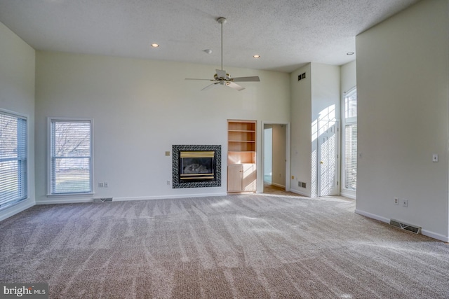 unfurnished living room with light carpet, a textured ceiling, built in features, a towering ceiling, and a high end fireplace