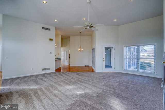 unfurnished living room featuring ceiling fan with notable chandelier, carpet floors, and a high ceiling