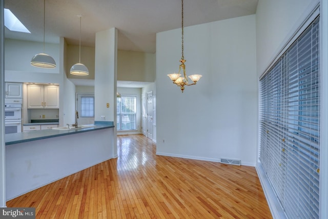 kitchen featuring sink, white double oven, white cabinetry, hanging light fixtures, and a towering ceiling