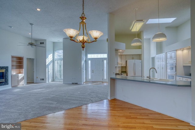 kitchen with a towering ceiling, sink, hanging light fixtures, light carpet, and white appliances