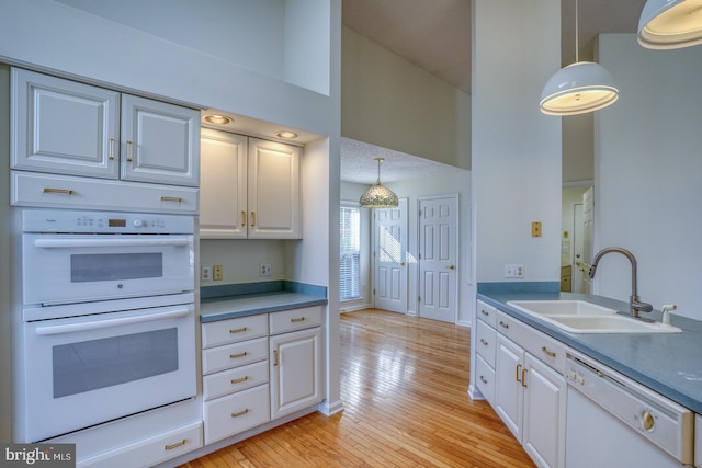 kitchen featuring white appliances, light hardwood / wood-style floors, sink, and hanging light fixtures