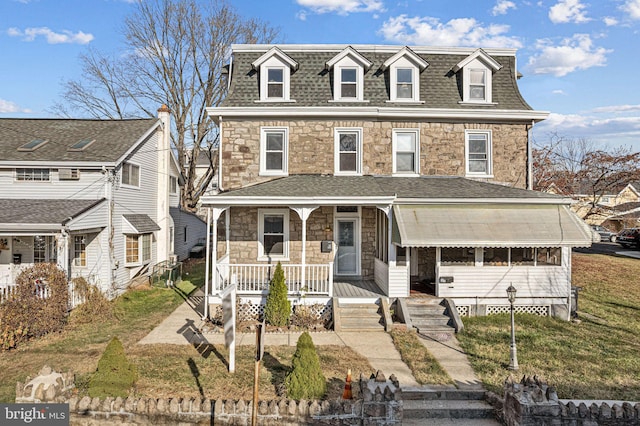 second empire-style home featuring stone siding, a shingled roof, and a porch