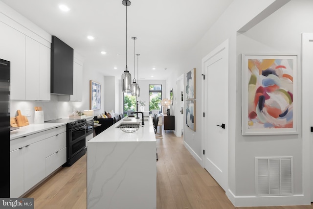 kitchen featuring pendant lighting, sink, white cabinets, a center island with sink, and range with two ovens