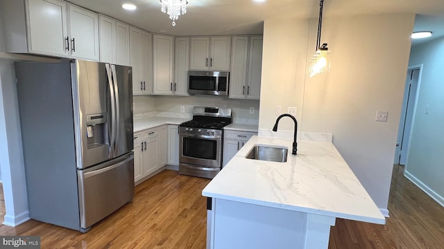 kitchen with sink, stainless steel appliances, wood-type flooring, light stone countertops, and decorative light fixtures