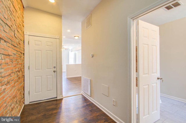 corridor with brick wall and dark hardwood / wood-style flooring