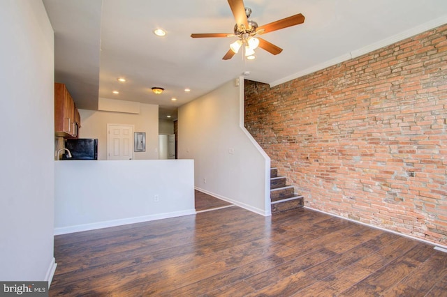 unfurnished living room featuring dark wood-type flooring, ceiling fan, and brick wall