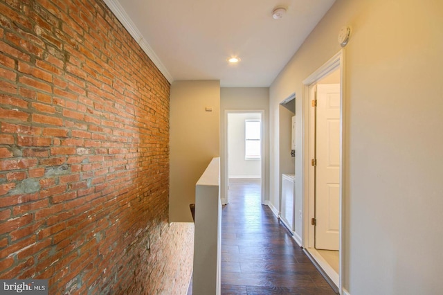 corridor with dark wood-type flooring, ornamental molding, and brick wall