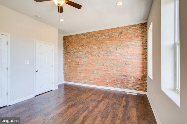 spare room with dark hardwood / wood-style flooring, ceiling fan, and brick wall