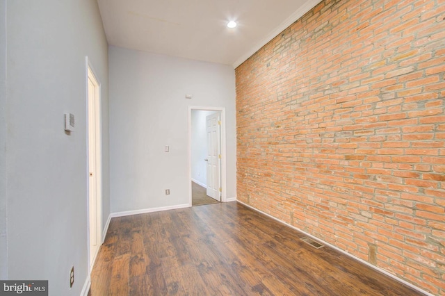 spare room featuring brick wall and dark wood-type flooring