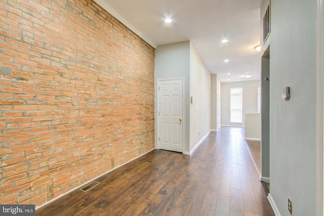 corridor with brick wall and dark hardwood / wood-style flooring