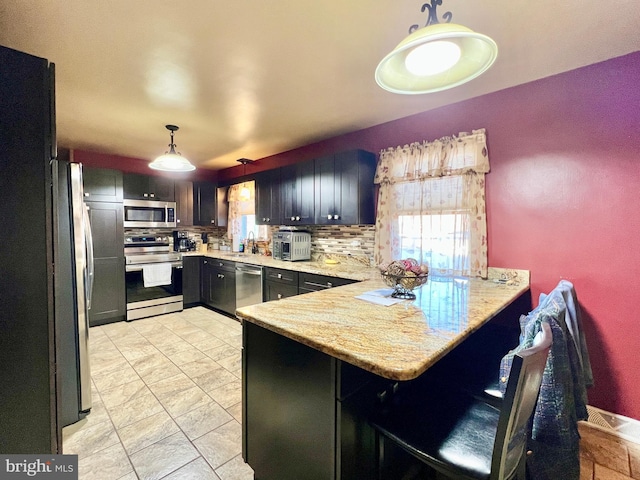 kitchen with sink, appliances with stainless steel finishes, light stone counters, decorative light fixtures, and kitchen peninsula