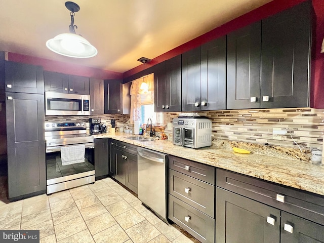 kitchen featuring sink, light stone counters, tasteful backsplash, decorative light fixtures, and appliances with stainless steel finishes