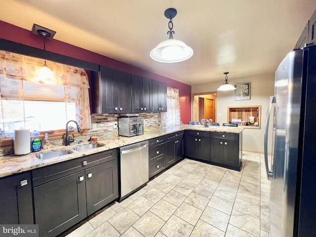 kitchen with sink, stainless steel appliances, light stone countertops, decorative light fixtures, and kitchen peninsula