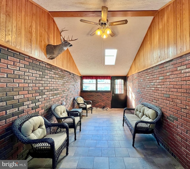 sitting room with vaulted ceiling, a textured ceiling, wooden walls, ceiling fan, and brick wall