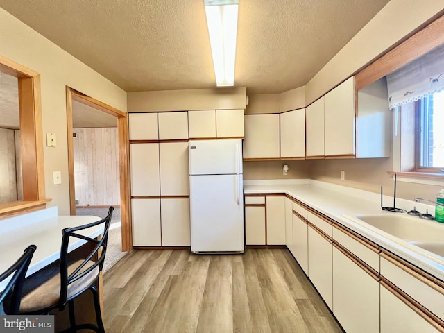 kitchen with white fridge, a textured ceiling, white cabinets, and light hardwood / wood-style floors