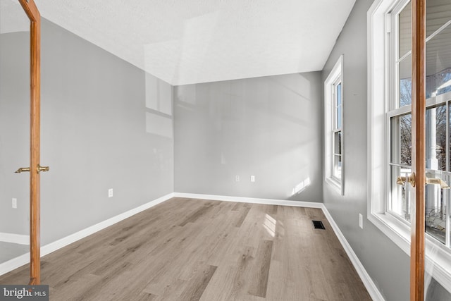 empty room with a textured ceiling and light hardwood / wood-style floors